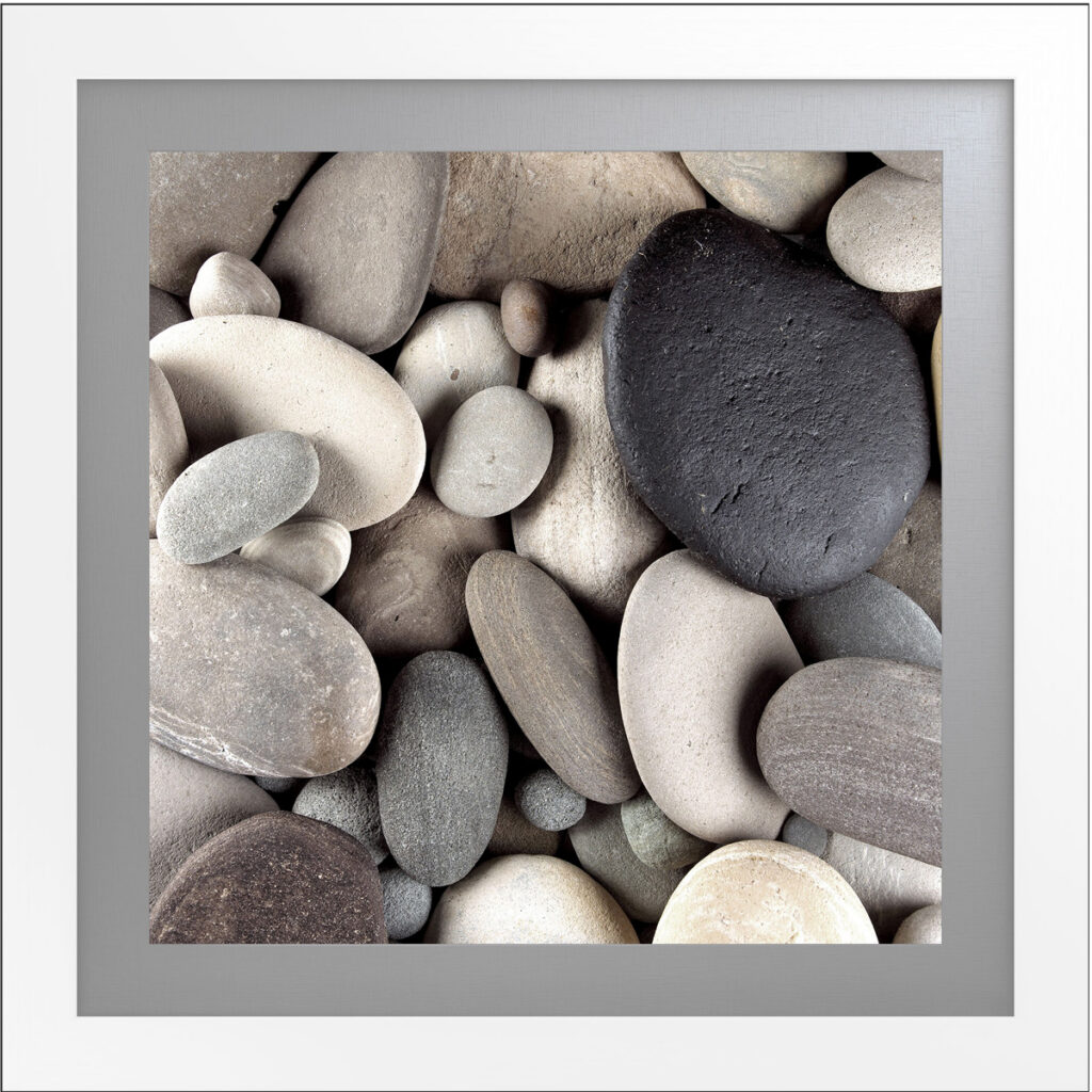 Pebble arrangement artwork with neutral tones and black stone accent, framed in white.
