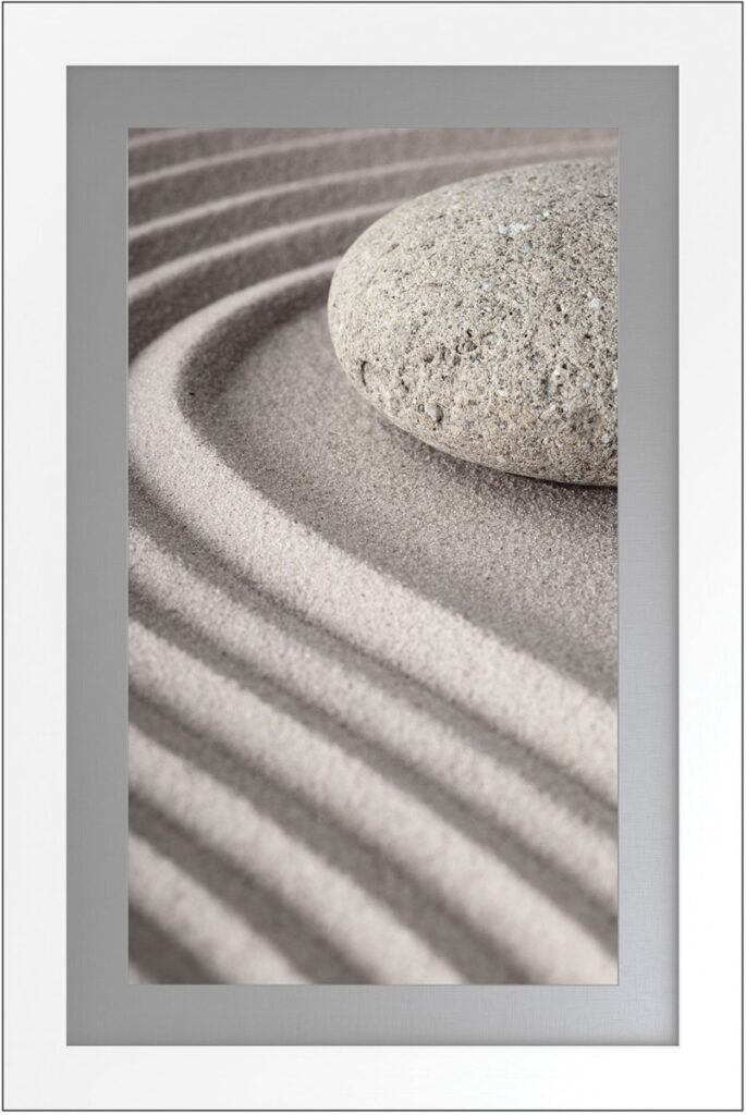 Serene sand art with a smooth stone, framed in white, perfect for calming interior decor.